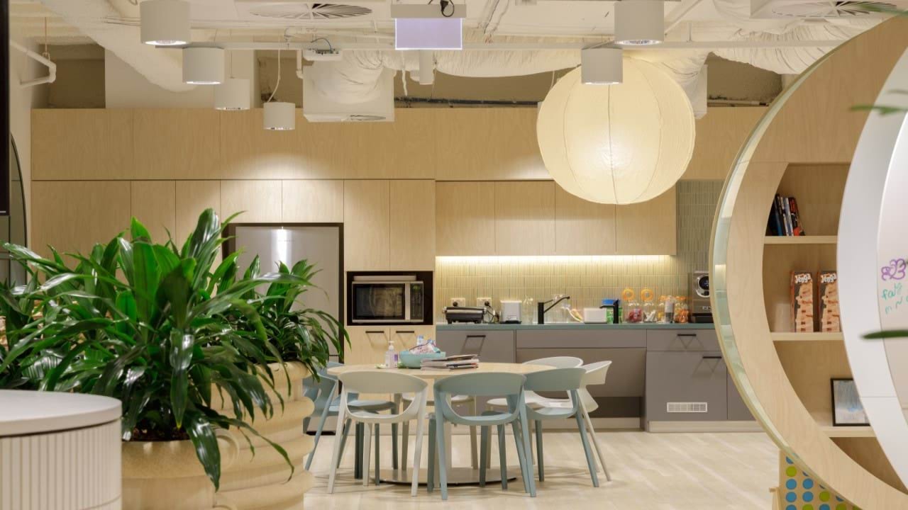 Large, bright kitchen area. Modern with exposed ceiling, plants in the foreground, and a large round table.