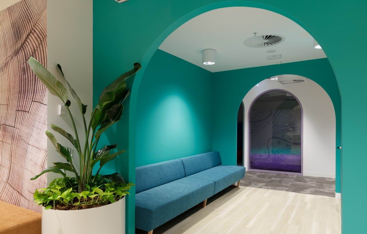 Couch area with wooden floors, teal walls with curved entranceways and green potted plant.